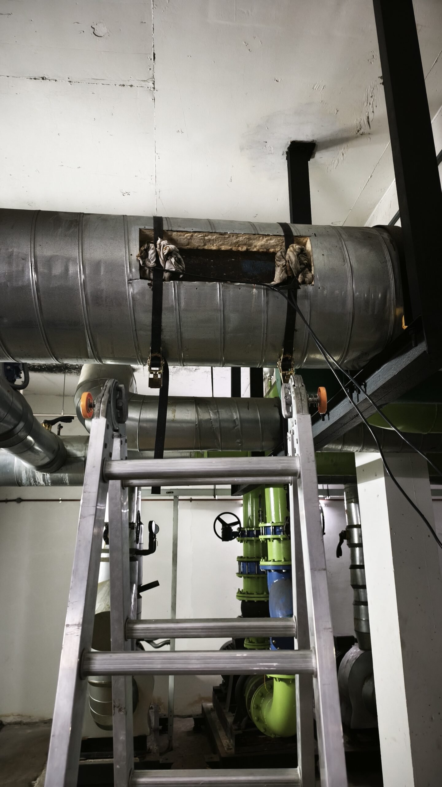 Clamp-on ultrasonic flow transducers secured with ratchet straps to a large-bore chilled water pipe, with the insulation opened at the measurement point in a building plant room
