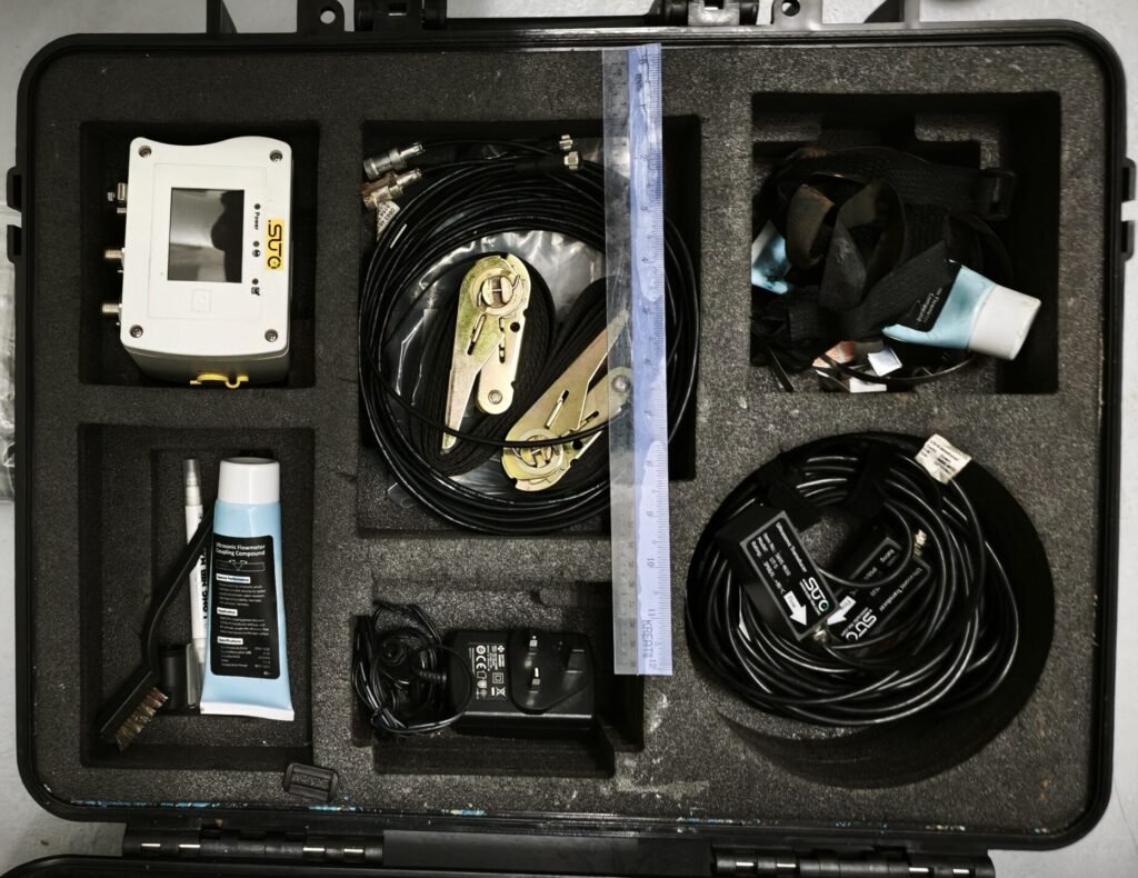 SUTO clamp-on ultrasonic flow meter kit in its transit case, showing the transmitter, transducer leads, mounting straps and acoustic coupling compound