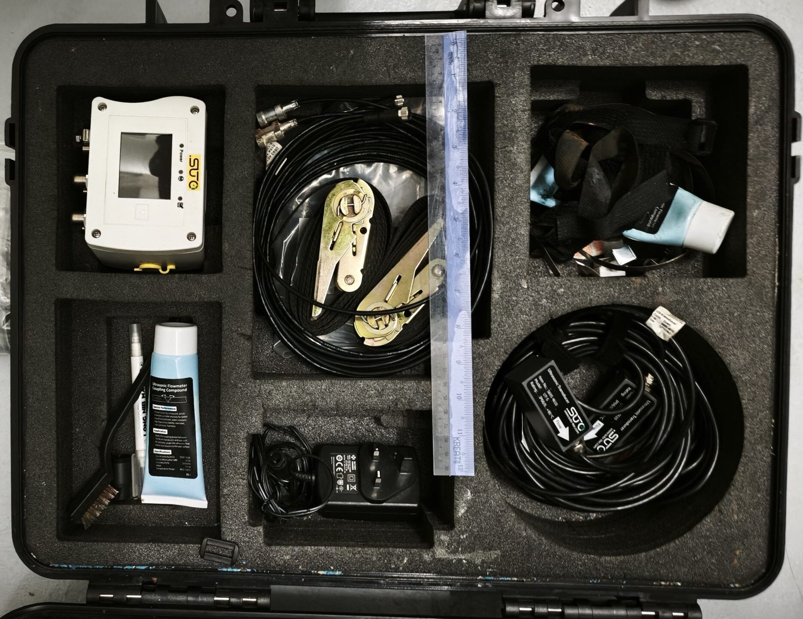 SUTO clamp-on ultrasonic flow meter kit in its transit case, showing the transmitter, transducer leads, mounting straps and acoustic coupling compound
