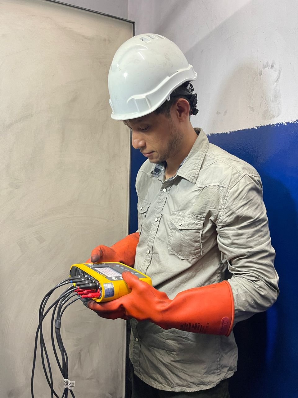 Innovast engineer holding a three-phase power quality analyser with test leads connected, wearing insulated gloves and a hard hat