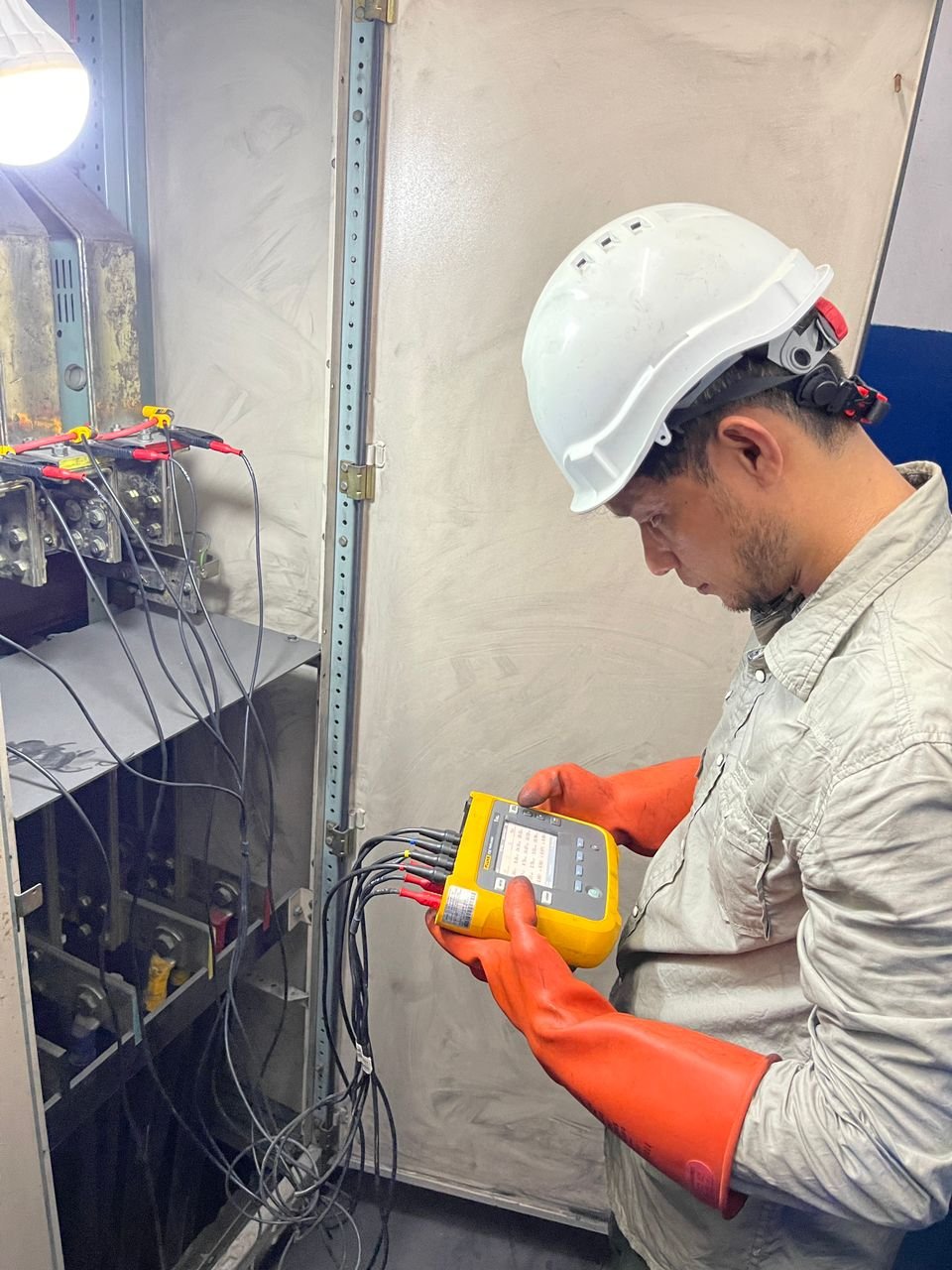 Power quality analyser connected to an open low-voltage switchboard during an energy audit, with voltage leads landed on the busbars