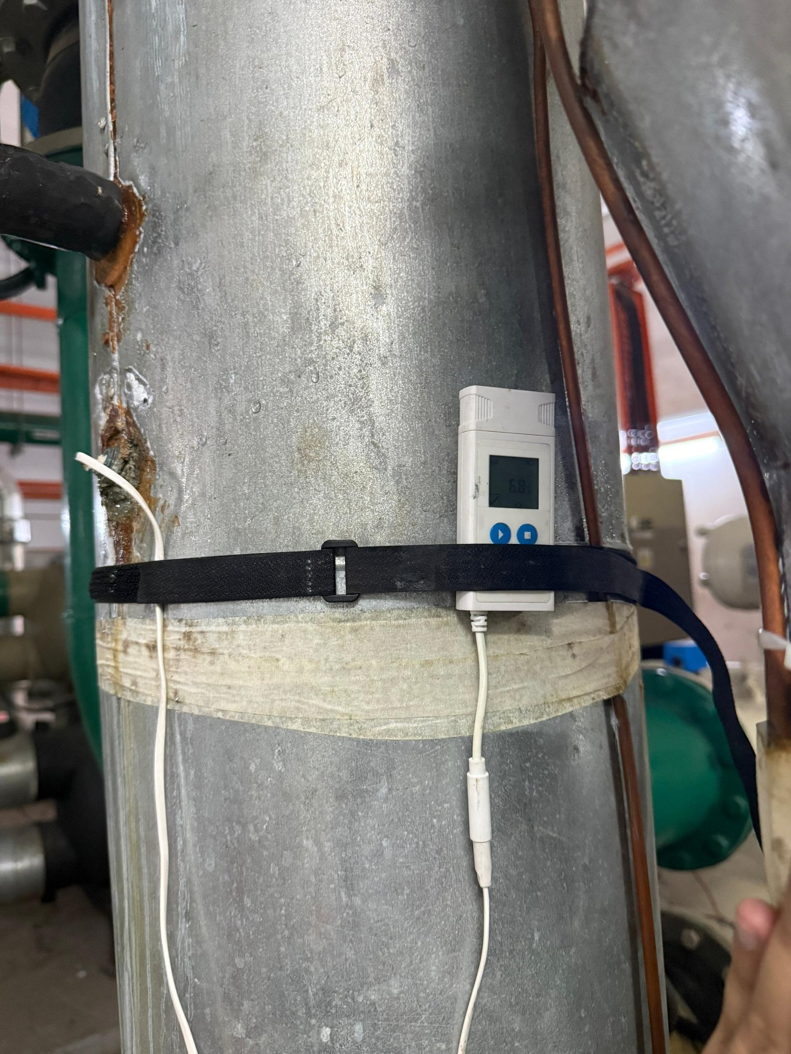 Data logger strapped to a vertical insulated chilled water riser, recording pipe surface temperature during an energy audit