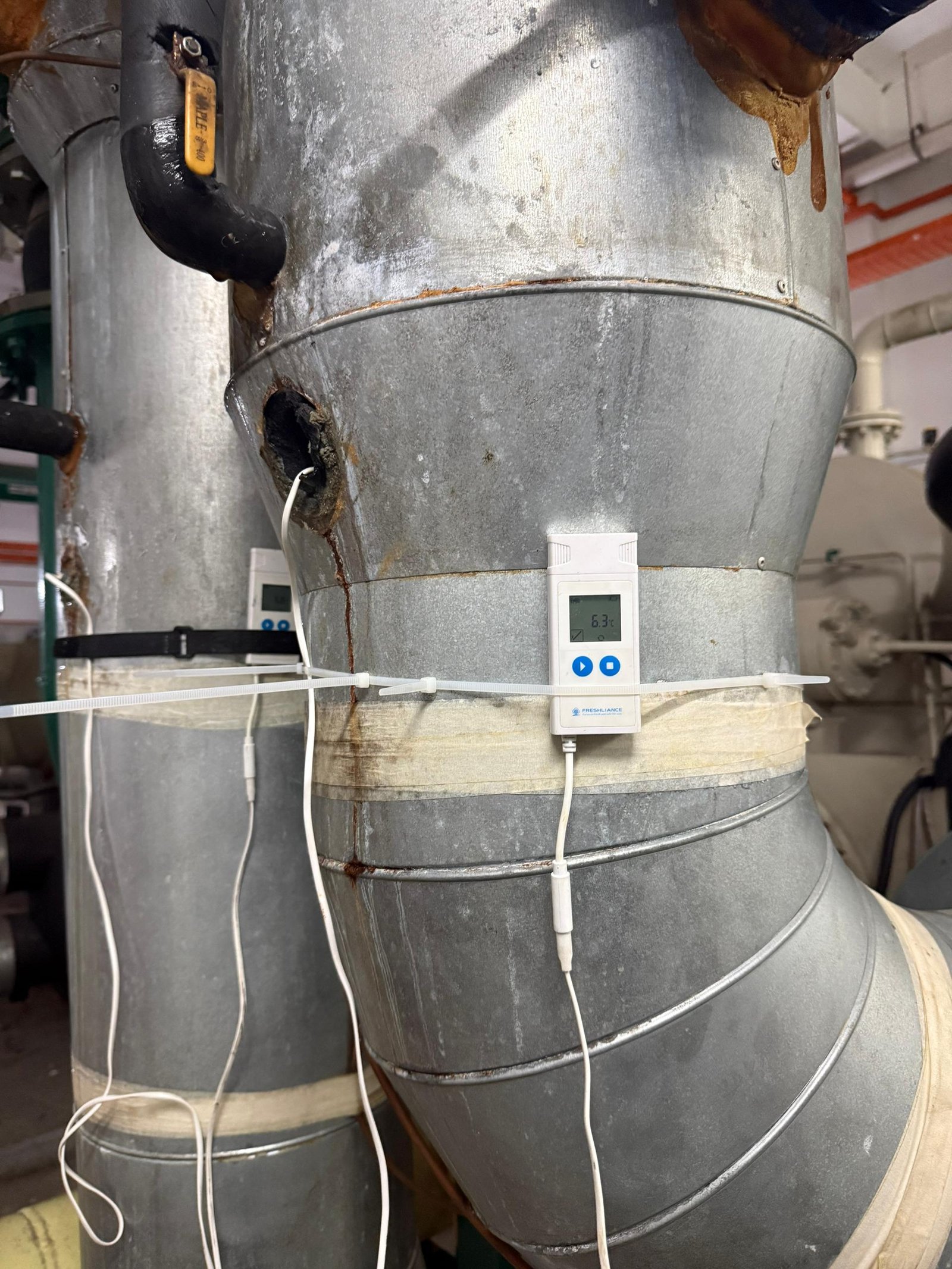 Two temperature loggers fitted to insulated chilled water pipework at an elbow, secured with cable ties at the insulation break